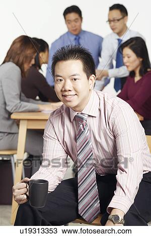 Stock Image - Portrait of a businessman sitting on a chair holding a coffee cup. Fotosearch