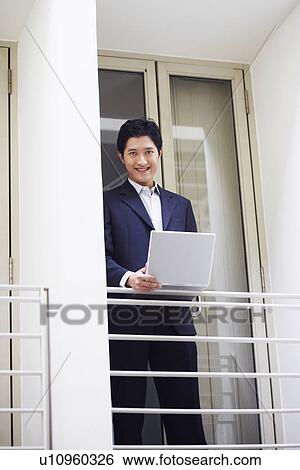Portrait of a businessman standing at the doorway of an office and using a laptop View Large Photo Image Stock Photograph - Portrait of a businessman standing at the doorway of an office and using a laptop. Fotosearch