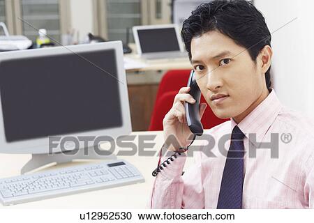 Stock Image - Portrait of a businessman talking on the telephone in an office. Fotosearch