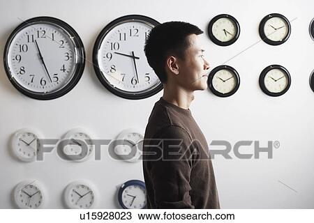 Side profile of a businessman standing in front of clocks on the wall View Large Photo Image Stock Image - Side profile of a businessman standing in front of clocks on the wall. Fotosearch