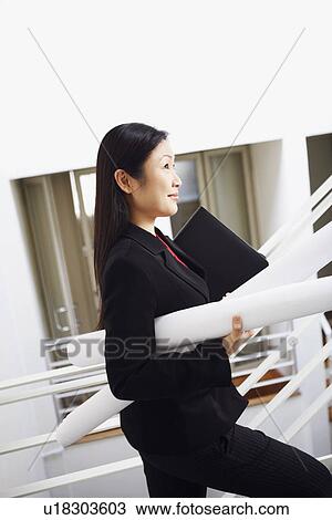 Stock Image - Side profile of a businesswoman carrying rolled charts and smiling. Fotosearch