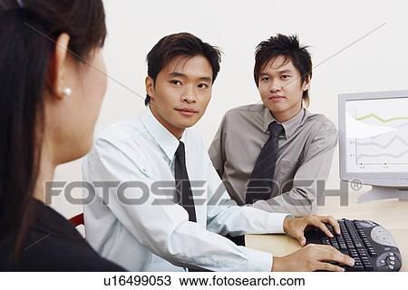 Stock Image - Two businessmen and a businesswoman sitting together in an office. Fotosearch