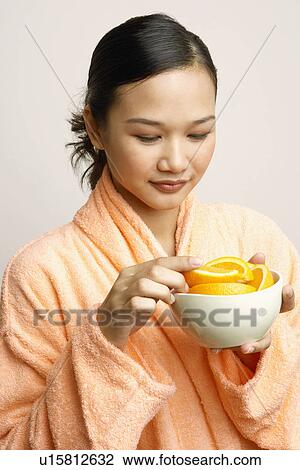 Stock Image - Close-up of a young woman holding a bowl of orange slices. Fotosearch