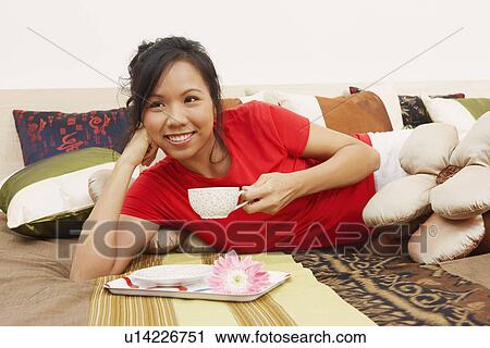 Stock Image - Close-up of a young woman lying on the bed and holding a cup of tea. Fotosearch