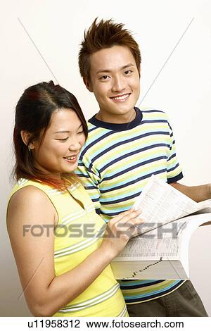 Stock Image - Portrait of a young man and a young woman holding a directory and smiling. Fotosearch
