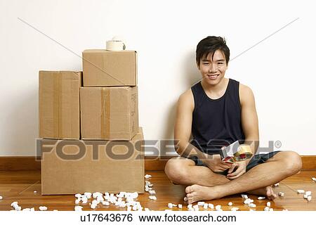 Stock Photograph - Portrait of a young man sitting on the floor and holding a tape dispenser. Fotosearch