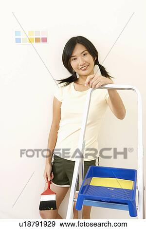 Stock Photo - Portrait of a young woman holding a paintbrush and smiling. Fotosearch