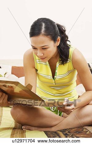 Young woman sitting on the bed and looking at a box of chocolates View Large Photo Image Picture - Young woman sitting on the bed and looking at a box of chocolates. Fotosearch