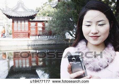 Stock Photo - Close-up of a young woman looking at a mobile phone smiling. Fotosearch