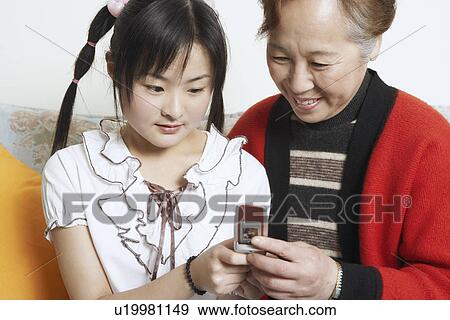 Close-up of a young woman with her grandmother holding a mobile phone View Large Photo Image Stock Photo - Close-up of a young woman with her grandmother holding a mobile phone. Fotosearch