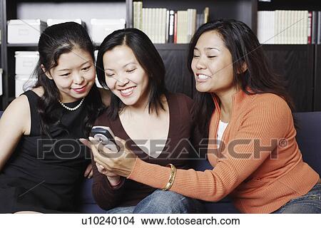 Picture - Close-up of three friends looking at a mobile phone smiling. Fotosearch