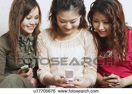 Stock Photograph - Close-up of three young women looking at a mobile phone. Fotosearch