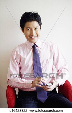 Portrait of a businessman holding a hand-held device and smiling View Large Photo Image Stock Image - Portrait of a businessman holding a hand-held device and smiling. Fotosearch