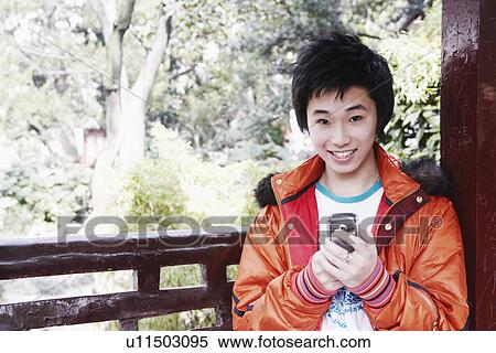 Portrait of a teenage boy holding a mobile phone smiling View Large Photo Image Stock Photography - Portrait of a teenage boy holding a mobile phone smiling. Fotosearch