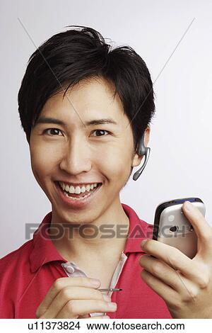 Portrait of a young man smiling and holding a personal data assistant View Large Photo Image Picture - Portrait of a young man smiling and holding a personal data assistant. Fotosearch