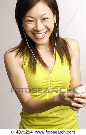 Picture - Portrait of a young woman holding a mobile phone and listening to music. Fotosearch