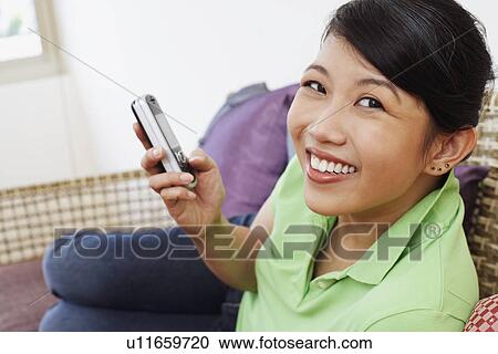Portrait of a young woman holding a mobile phone and smiling View Large Photo Image Stock Image - Portrait of a young woman holding a mobile phone and smiling. Fotosearch