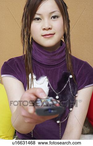 Stock Photo - Portrait of a young woman holding a remote control. Fotosearch