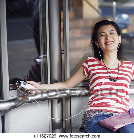 Portrait of a young woman listening to an MP3 player and smiling View Large Photo Image Stock Photo - Portrait of a young woman listening to an MP3 player and smiling. Fotosearch