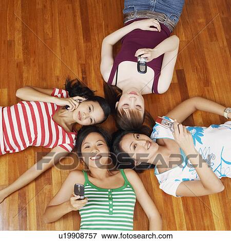Stock Photo - Portrait of four young women lying on a hardwood floor and holding mobile phones. Fotosearch