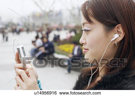 Side profile of a young woman listening at an MP3 player View Large Photo Image Stock Photograph - Side profile of a young woman listening at an MP3 player. Fotosearch