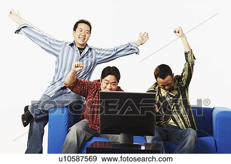Three young men sitting on a couch in front of a flat screen monitor View Large Photo Image Stock Photo - Three young men sitting on a couch in front of a flat screen monitor. Fotosearch