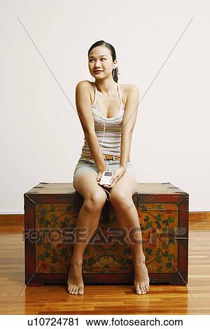 Stock Image - Young woman sitting on a trunk and listening to music. Fotosearch