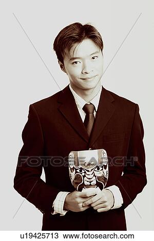 Stock Image - Portrait of a businessman holding a mask and smiling. Fotosearch