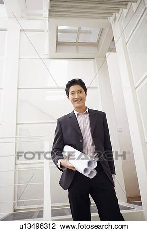Stock Image - Portrait of a businessman holding blueprints and smiling. Fotosearch