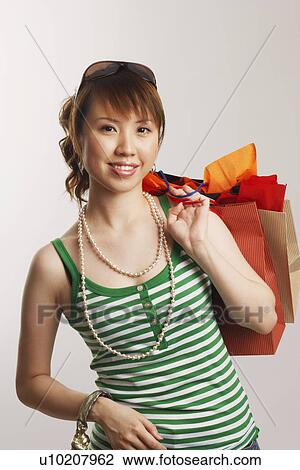 Stock Image - Portrait of a young woman carrying shopping bags and smiling. Fotosearch