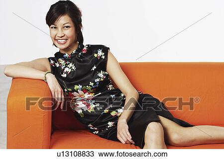 Stock Image - Portrait of a young woman sitting on a couch smiling. Fotosearch