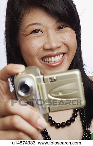 Stock Image - Portrait of a young woman smiling and taking a photograph. Fotosearch