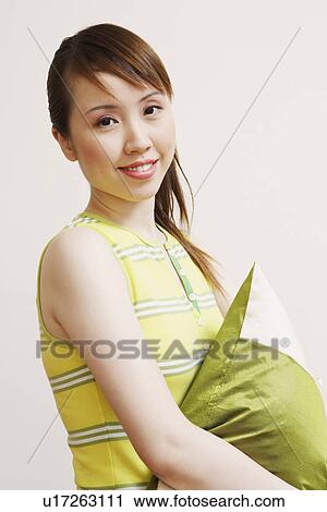 Stock Image - Side profile of a young woman holding a cushion and smiling. Fotosearch