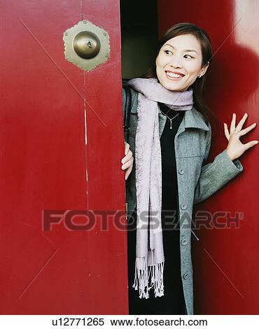 Stock Photography - Close-up of a young woman looking out of an open door. Fotosearch