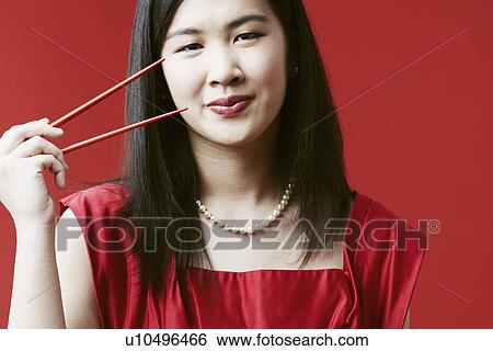 Stock Photograph - Portrait of a young woman holding chopsticks. Fotosearch