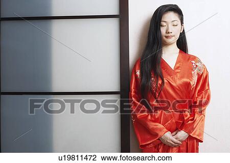 Stock Image - Close-up of a young woman leaning against a wall with her eyes closed. Fotosearch