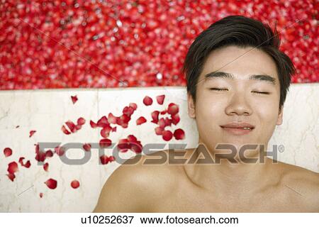 Stock Photo - High angle view of a young man lying on the floor near a hot tub filled with rose petals. Fotosearch