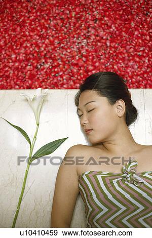Stock Photo - High angle view of a young woman lying on the floor near a hot tub filled with rose petals. Fotosearch