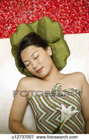 Stock Photo - High angle view of a young woman lying on the floor near a hot tub with her eyes closed. Fotosearch