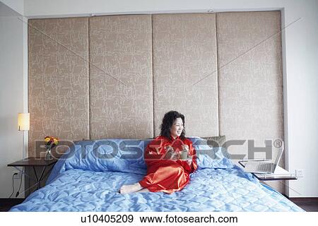 Mature woman reclining on the bed with a cup of tea smiling View Large Photo Image Stock Photo - Mature woman reclining on the bed with a cup of tea smiling. Fotosearch