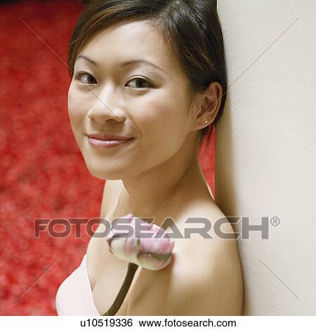 Stock Photograph - Portrait of a young woman leaning against a wall near a hot tub filled with rose petals. Fotosearch
