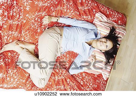 Stock Image - Portrait of a young woman lying on the bed smiling. Fotosearch