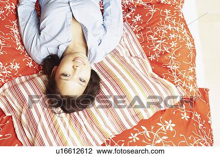 Stock Image - Portrait of a young woman lying on the bed smiling. Fotosearch