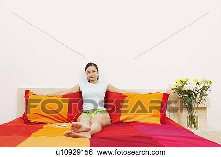 Portrait of a young woman reclining on the bed and listening to music on headphones View Large Photo Image Stock Photograph - Portrait of a young woman reclining on the bed and listening to music on headphones. Fotosearch