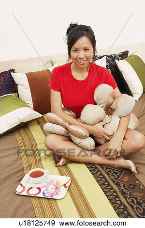 Portrait of a young woman sitting on the bed with cushions and smiling View Large Photo Image Stock Photo - Portrait of a young woman sitting on the bed with cushions and smiling. Fotosearch