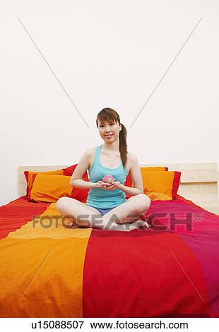 Portrait of a young woman sitting cross-legged on the bed and holding a lotus flower View Large Photo Image Stock Photo - Portrait of a young woman sitting cross-legged on the bed and holding a lotus flower. Fotosearch