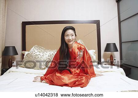 Stock Photo - Young woman sitting on the bed. Fotosearch