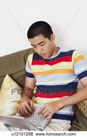 High angle view of a young man sitting on a couch and using a laptop View Large Photo Image Stock Photo - High angle view of a young man sitting on a couch and using a laptop. Fotosearch