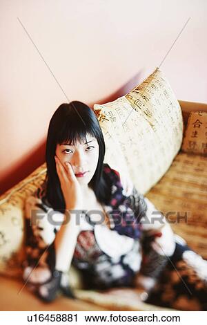 Stock Image - High angle view of a young woman sitting on a couch. Fotosearch