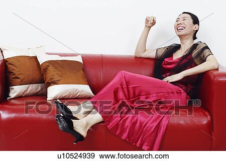Stock Photo - Mid adult woman reclining on a couch and laughing with her eyes closed. Fotosearch